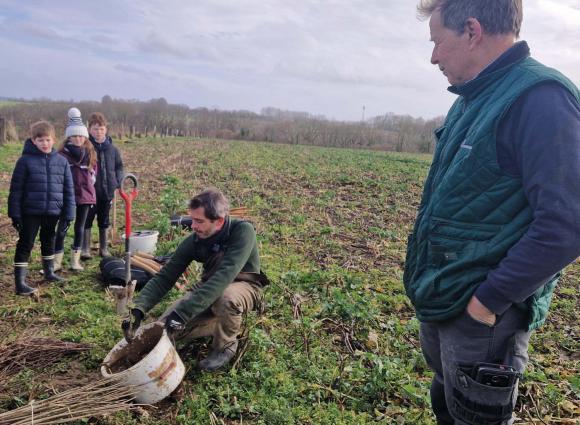 Olivier Tassel (au premier plan) écoute les consignes de plantation que Benoit Caumont, spécialiste en agroforesterie, partage avec les enfants. 